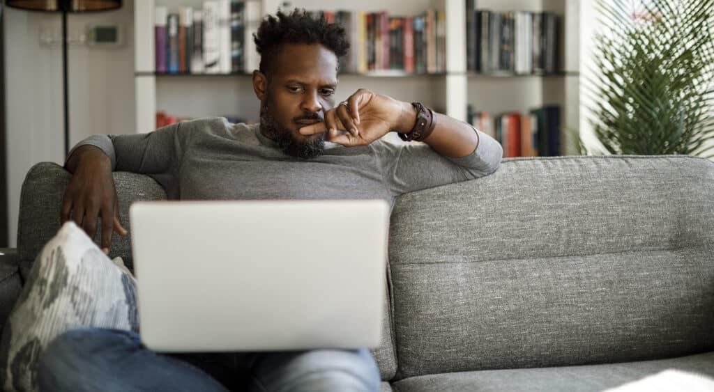 Man sitting on couch at home starting pensively at laptop