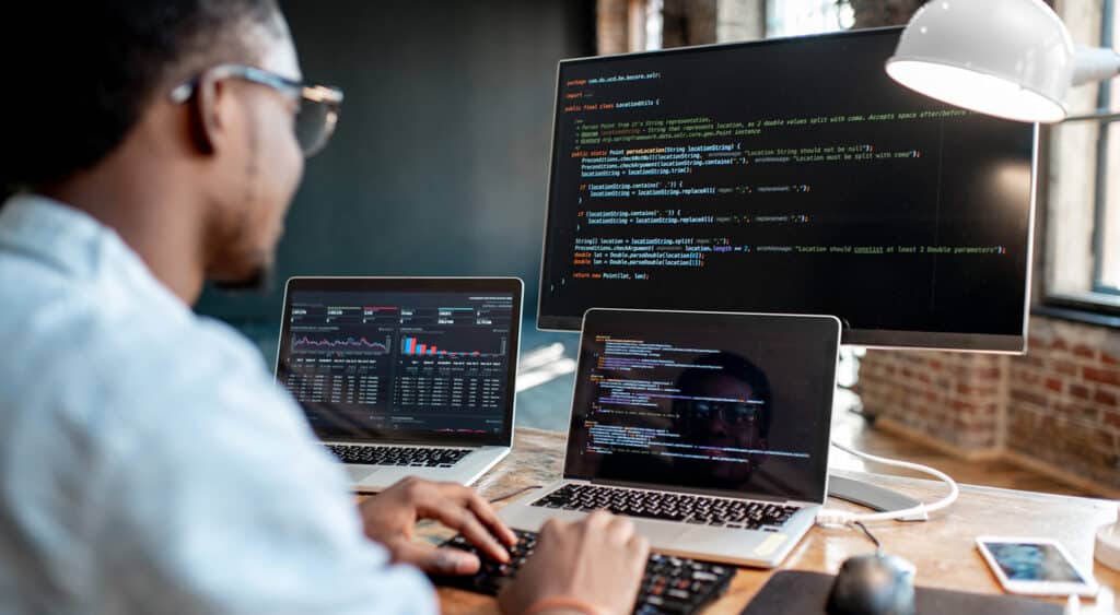 Technical professional with two laptops and a large screen reviewing data