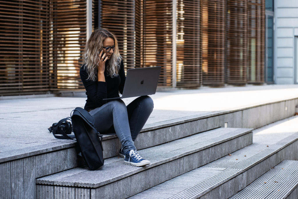 A woman sitting on the stairs with a laptop, talking on the phone.