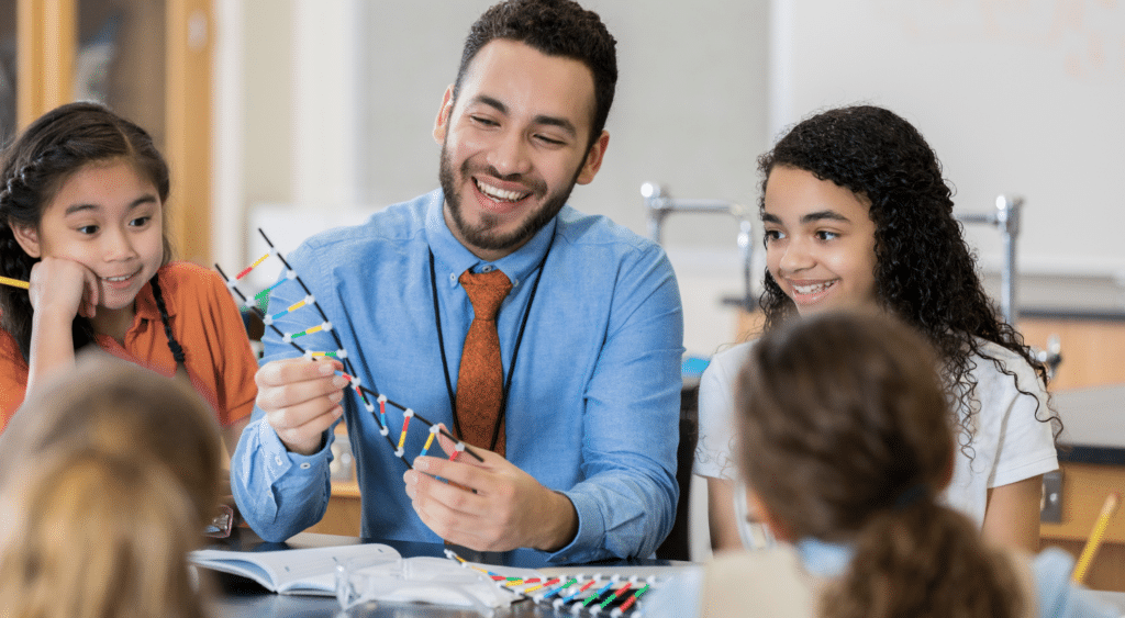 A teacher among elementary students, explaining a lesson with some materials.